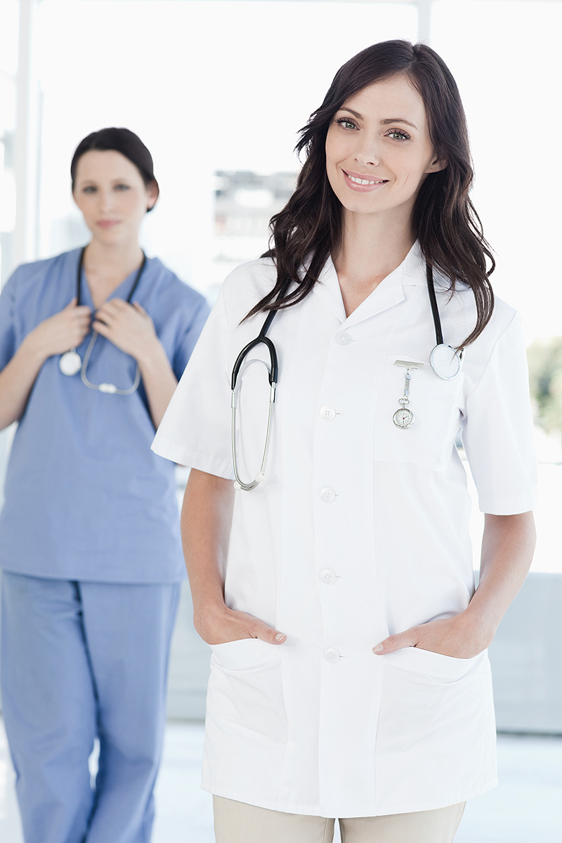 A smiling nurse standing upright while her colleague is behind her